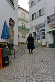 La femme en noir dans la rue pavée, Nazaré, Portugal.